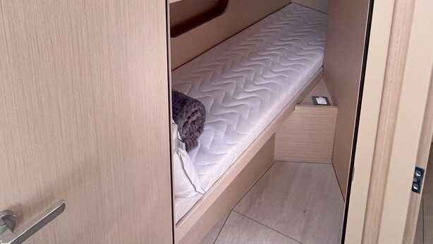 Une petite chambre avec un lit superposé, une lucarne, un petit compartiment de rangement et une poignée de porte.