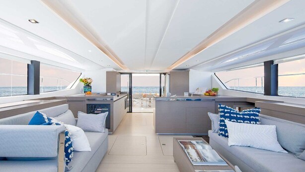 A modern yacht interior with a central dining area, two seating areas with sofas, a kitchen counter, and a view of the sea. - Sun-Kissed Sailing Adventure in Islas Sarónicas (Piraeus)