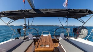 Cubierta de barco con una mesa de madera, dos asientos blancos acolchados, un timón y una bandera.