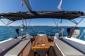 A boat deck with a wooden table, two white cushioned seats, a steering wheel, and a flag. - Sun-Kissed Sailing Adventure in Zadar, Croatia (Zadar)