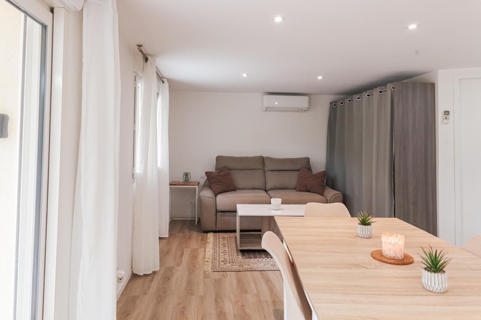 A modern living room with a sofa, a dining table with candles, and a small side table.
