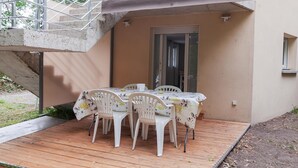 Une terrasse avec une table et des chaises, une plateforme en bois et un escalier en métal.
