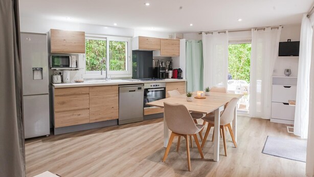 Une cuisine moderne avec des meubles en bois, des appareils en acier inoxydable et un coin repas comprenant une table et des chaises.