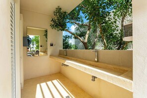 A bathroom with a beige sink, a mirror, and a view of trees and a building outside. - Rooftop Penthouse | Work Remotely in Akumal (AKUMAL)