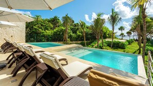 A poolside area with lounge chairs and umbrellas, surrounded by lush greenery and palm trees. - Rooftop Penthouse in Akumal jungle — steps to the beach (AKUMAL)