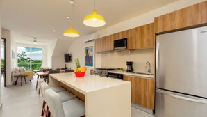 A modern kitchen with a large island, wooden cabinets, stainless steel appliances, and a dining area with bar stools. - Rooftop Penthouse in Akumal jungle — steps to the beach (AKUMAL)