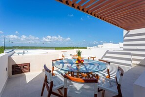 A glass-top table with chairs, a pineapple, and fruit on a rooftop terrace with a clear sky. - Rooftop Penthouse | Work Remotely in Akumal (AKUMAL)