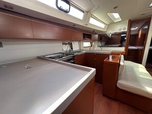 A compact kitchen with a countertop, wooden cabinets, and a small seating area with a cushioned bench. - Sun-Kissed Sailing Adventure in Islas Sarónicas (Alimos)