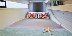 Une chambre à coucher de taille réduite, avec un lit superposé, deux coussins décorés de motifs de papillons, une étoile de mer en guise de décoration et une bibliothèque remplie de livres.