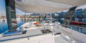 Eine moderne Yacht, ausgestattet mit einer Steuerung, einem Spülbecken und einem kleinen Tisch mit Blumenarrangements. Die Yacht liegt in einer Marina vor Anker, im Hintergrund sind weitere Boote und Gebäude zu sehen.