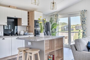 Een moderne keuken met witte kasten, een ingebouwde oven en een zithoek met een grijze bank en een kleine tafel.