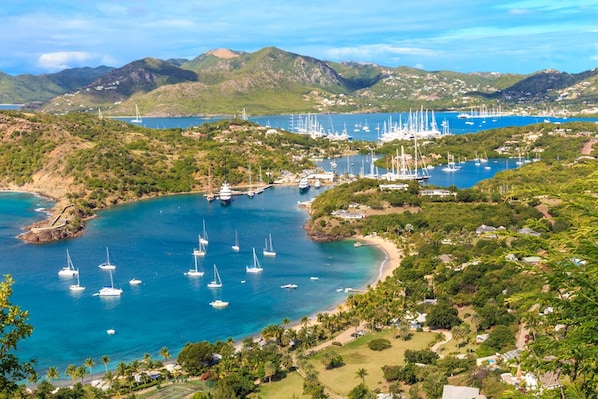 A coastal area with numerous sailboats docked in a marina, surrounded by lush greenery and hills.