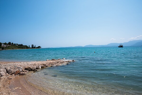 Une vue dégagée sur la côte, avec un rivage rocheux, une mer calme et des montagnes à l’horizon.