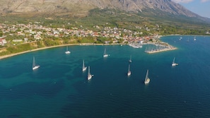 Vue aérienne d’une ville côtière avec un port de plaisance, des bateaux et une chaîne de montagnes en arrière-plan.