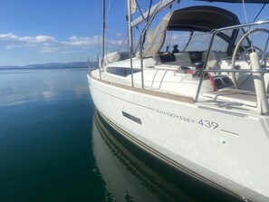 A sailboat named SUN ODYSSEY 439 docked at a marina with calm waters and distant mountains.