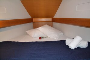 Ein Einzelbett mit Holz-Kopfteil, weißen Kissen, einer dunkelblauen Bettdecke, einer roten Rose und gefalteten weißen Handtüchern.