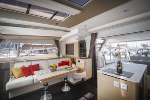 A yacht interior with a dining area, a sofa with cushions, a small TV, and a minibar. - Sun-Kissed Sailing Adventure in the Ionian Islands, Lefkada (Lefkada)