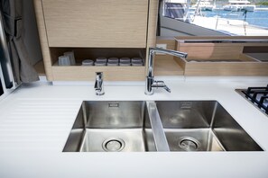 Eine moderne Küche mit Spüle aus Edelstahl, zwei Wasserhähnen und einem Holzschrank darüber.