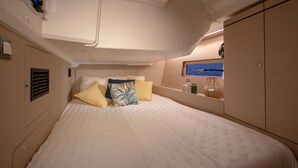 Quarto com cama, almofadas, uma estante com objetos e vista para o mar.