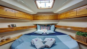 Um camarote de barco compacto com cama, armários de madeira, um claraboia e uma pequena planta.