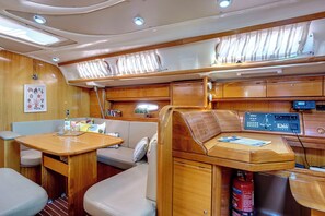 A cabin with a wooden interior, a control panel, a table with a chair, and a cushioned seating area. - Sun-Kissed Sailing Adventure in the Ionian Islands, Lefkada (Lefkada)