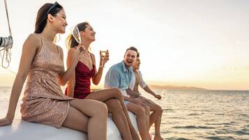 Un groupe de personnes se trouve sur un bateau, avec une vue sur la mer et un coucher de soleil en arrière-plan.