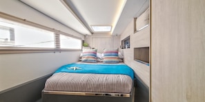 Ein schmales, gut beleuchtetes Zimmer mit einem Bett, einem Oberlicht und einem Fenster.