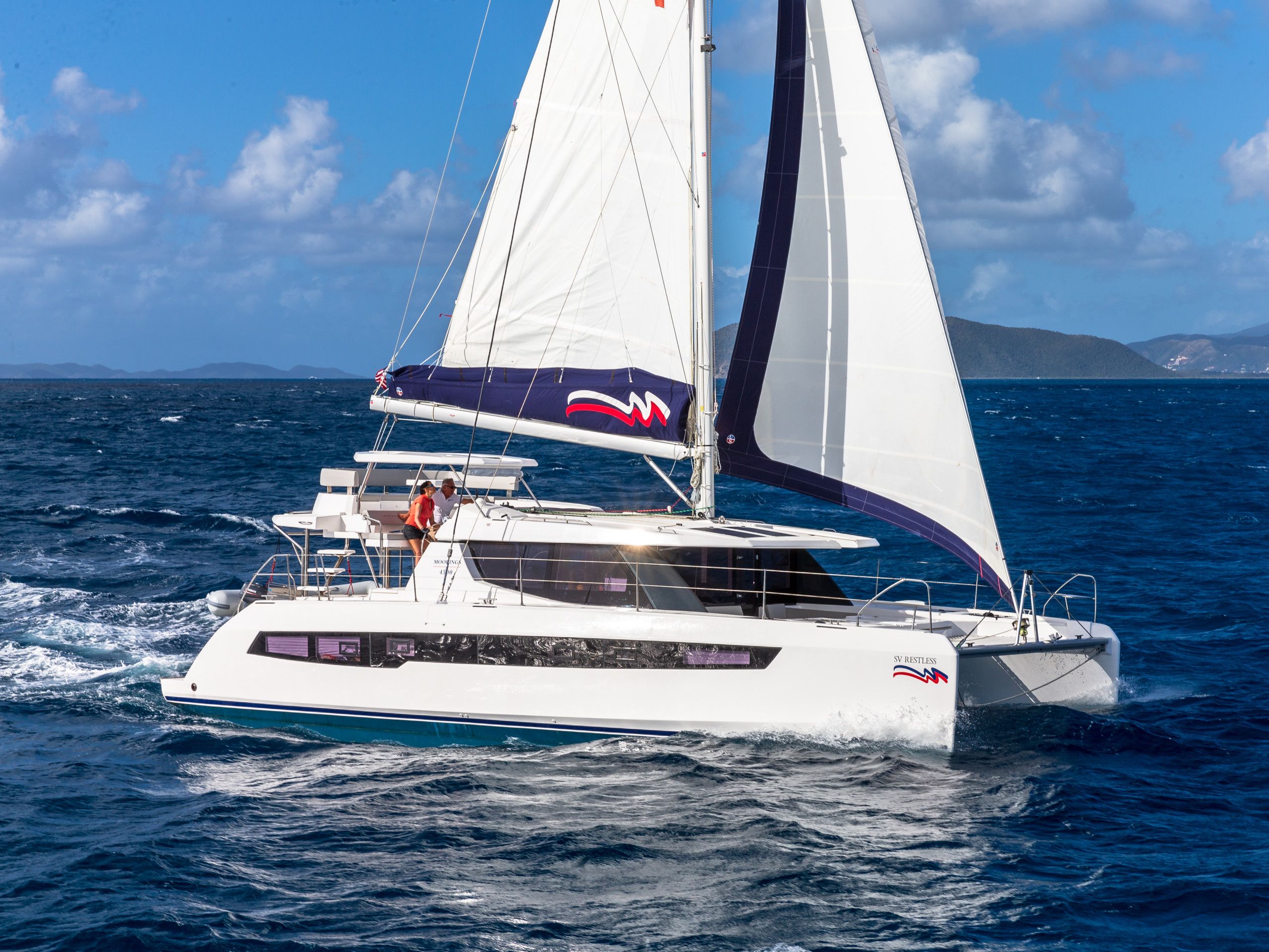 A white yacht with a cabin and a sail, sailing on the water.
