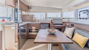 Ett modernt kök med vitvaror i rostfritt stål, en matplats med bord och stolar samt stora fönster med utsikt över havet.