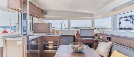 A modern kitchen with stainless steel appliances, a dining area with a table and seating, and large windows offering views of the sea.