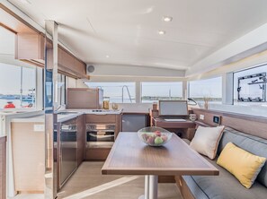 A modern kitchen with stainless steel appliances, a dining area with a table and seating, and large windows offering views of the sea. - Sun-Kissed Sailing Adventure in Islas Sarónicas (Alimos)