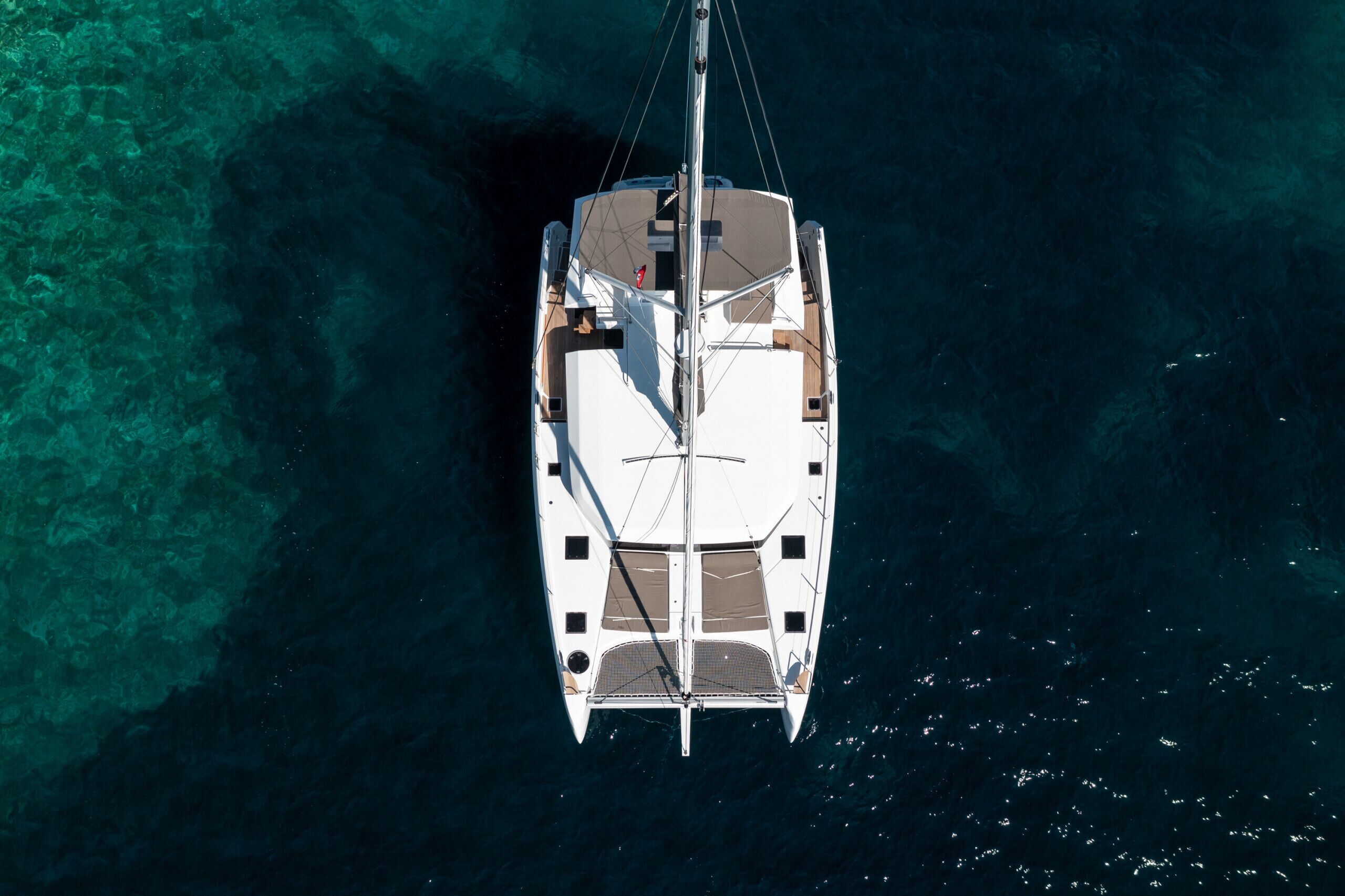An aerial view of a sailboat with a cabin and deck layout, surrounded by clear blue water.