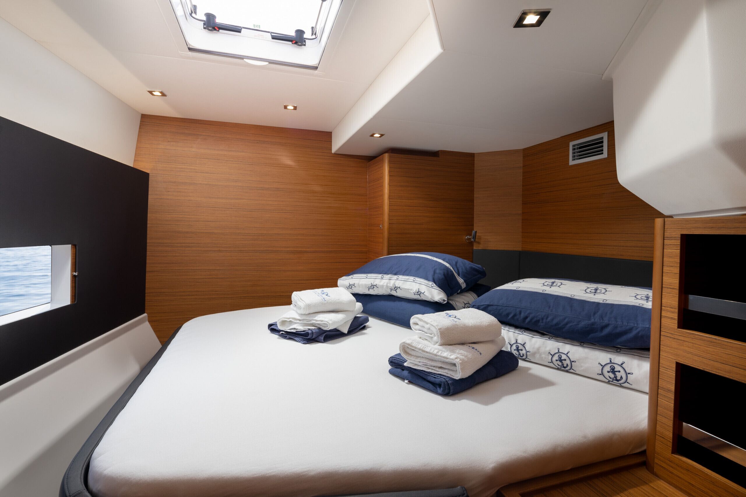 Une chambre à coucher de taille modeste, dotée d’un puits de lumière, d’un lit avec des serviettes soigneusement pliées et d’un mur en bois.
