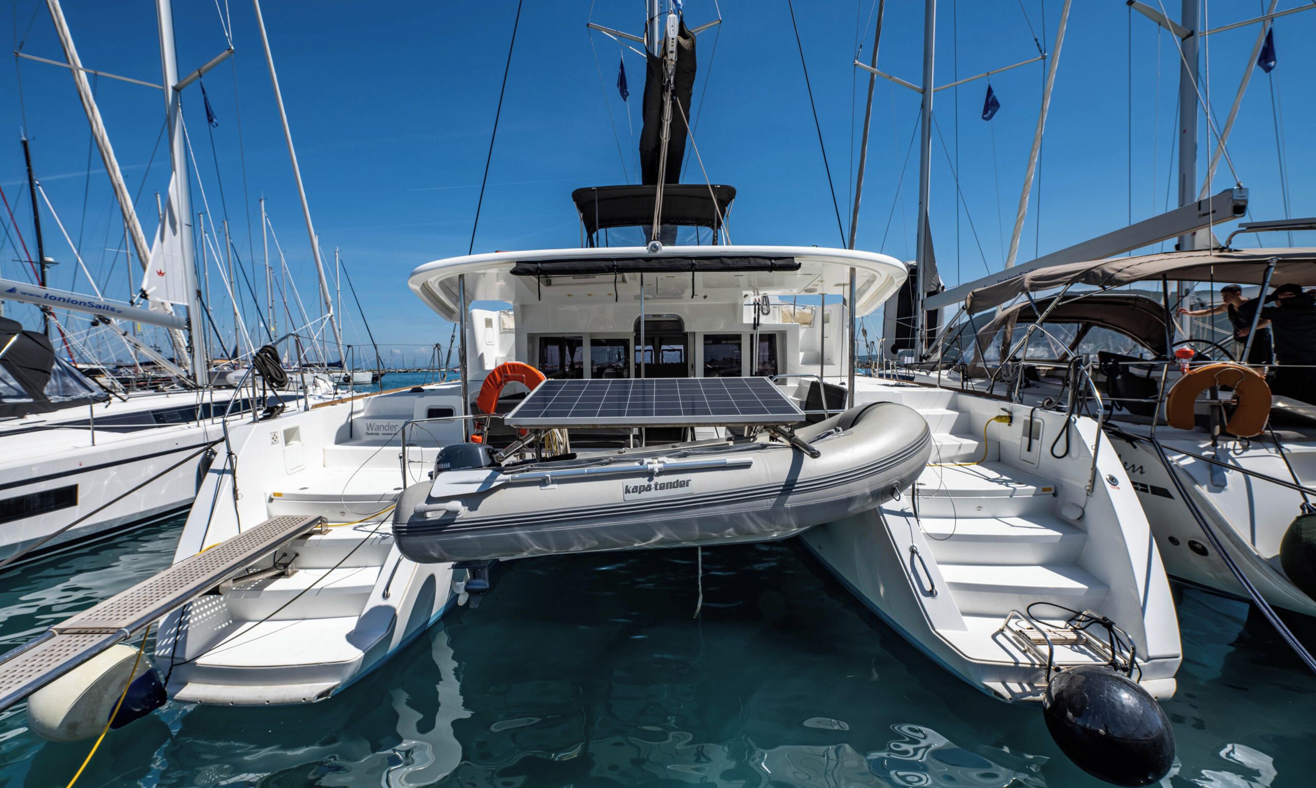 A marina with multiple boats docked, a central boat with a solar panel, and a clear blue sky.