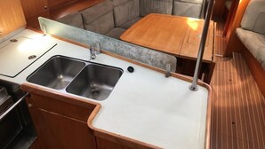 A compact kitchenette with a sink, a stove, and a small dining area with a table and bench. - Sun-Kissed Sailing Adventure in Tenerife, Islas Canarias (Las Galletas)