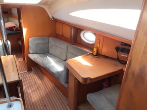 A compact interior with a cushioned seating area, a small table, and a window. - Sun-Kissed Sailing Adventure in Tenerife, Islas Canarias (Las Galletas)
