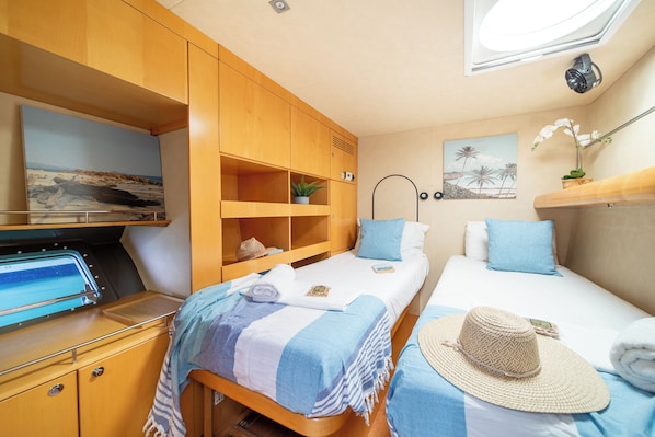 A compact bedroom with two beds, a wooden wardrobe, a small shelf with a plant, and a wall-mounted lamp.