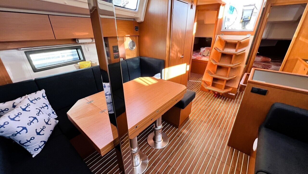 A compact interior with a dining table, cushioned seating, a small window, and a storage unit.