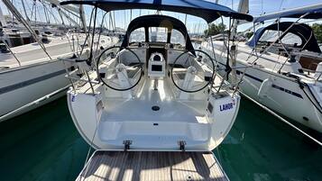 A sailboat docked at a marina with a covered deck area, a steering wheel, and a name 'LAHOR' on the side.