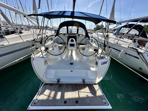 A sailboat docked at a marina with a covered deck area, a steering wheel, and a name 'LAHOR' on the side.