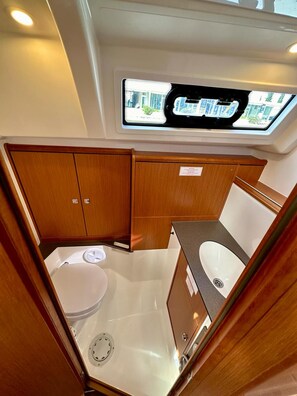 A compact bathroom with a toilet, sink, and vanity, featuring wooden cabinetry and a skylight. - Sun-Kissed Sailing Adventure in Zadar, Croatia (Bibinje)