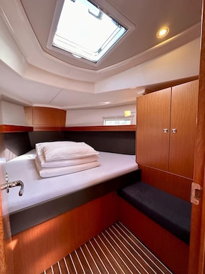 A compact cabin with a skylight, a bed with white linens, a small sink, and wooden cabinetry. - Sun-Kissed Sailing Adventure in Zadar, Croatia (Bibinje)