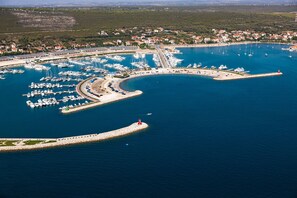 An aerial view of a marina with numerous boats docked, a lighthouse, and a coastal town in the background.