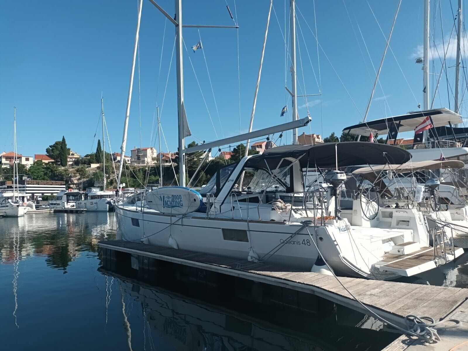 A marina with several sailboats docked, a wooden dock, and buildings in the background.