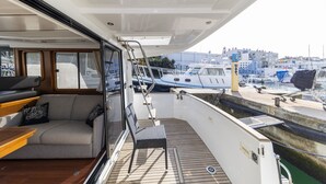 Terraza abierta con un sofá, una silla y una mesa, con vistas a un puerto deportivo con barcos y edificios.