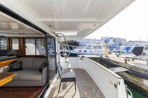 An open deck with a sofa, a chair, and a table, overlooking a marina with boats and buildings. - Sun-Kissed Sailing Adventure in Zadar, Croatia (Zadar)