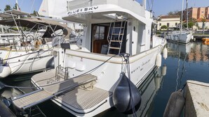 Un yate blanco llamado 'Blue Sky' amarrado en un puerto deportivo, con cubierta techada y una pequeña cabina.