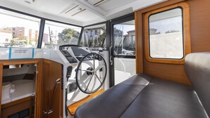 Interior de barco con timón, un armario de madera y vista al exterior.