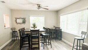 A dining area with a table, chairs, a ceiling fan, and large windows.