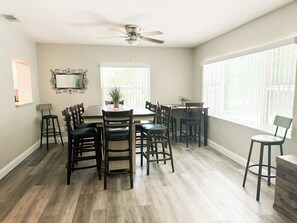 A dining area with a table, chairs, a ceiling fan, and large windows.